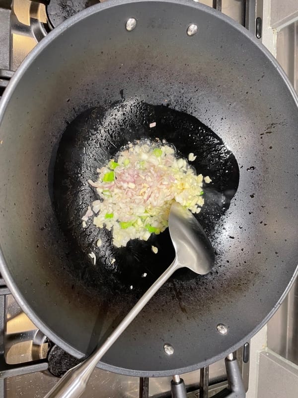 Calienta el aceite en un wok y saltea el ajo picado, la chalota y la cebolla verde picada a fuego medio-alto.