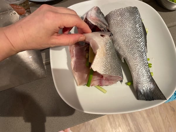 El pescado es bastante largo, por lo que lo cortamos por la mitad. Luego coloque el pescado sobre el jengibre y las cebolletas en el plato, y ponga algunas cebolletas y jengibre en la panza del pescado para eliminar el olor a pescado.