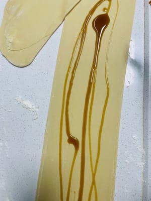 Extender la masa amasada en una lámina fina, pincelarla con una capa de jarabe de azúcar moreno líquido, luego enrollarla firmemente, asegurándose de que no queden huecos, y luego cortarla en trozos pequeños de unos 3 cm de largo.