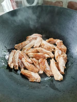 Dann die Hähnchenflügel hineingeben, bei schwacher Hitze braten