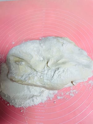 操作台上撤上干面粉防沾，将发酵好的面团拿出来，继续揉，排气。