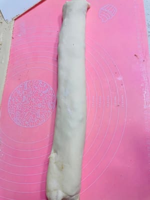 将涂抹好调料的面皮自一端向上折叠，均匀叠成3层，形成规整的长方形。接着，从长边一侧开始，紧密卷成直径约6厘米的长条状，确保层次紧实不松散，为后续造型与蒸制时保持美观层次打下基础。