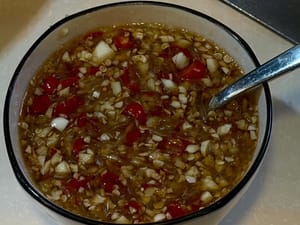 Campurkan bawang putih cincang, cabai cincang, air jeruk nipis, saus ikan, saus cabai manis Thailand, cuka putih, dan gula pasir untuk membuat saus asam manis.