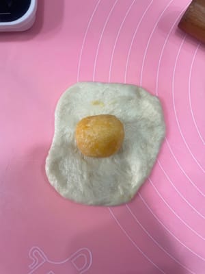 50g小餐包:
把面团压扁,包入约20g椰蓉馅,像包包子一样收口,一定要捏紧!不然烤的时候会爆馅。
收口朝下摆进烤盘,我用的28×28烤盘,每排3个,刚好放9个。