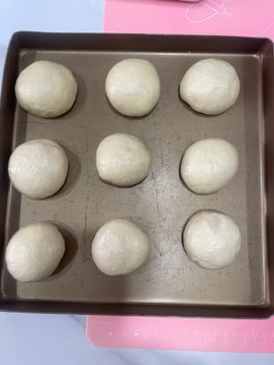 50g小餐包:
把面团压扁,包入约20g椰蓉馅,像包包子一样收口,一定要捏紧!不然烤的时候会爆馅。
收口朝下摆进烤盘,我用的28×28烤盘,每排3个,刚好放9个。