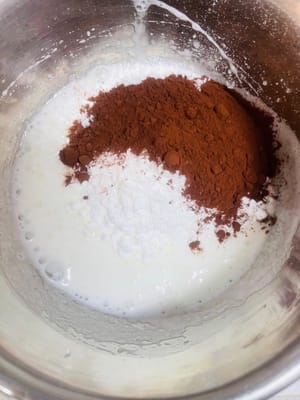 Preparazione della glassa: in una ciotola a parte, montare gli albumi con lo zucchero fino a ottenere una consistenza soda. Aggiungere quindi la polvere di mandorle e il cacao in polvere, mescolare bene e trasferire il composto in una sac à poche.