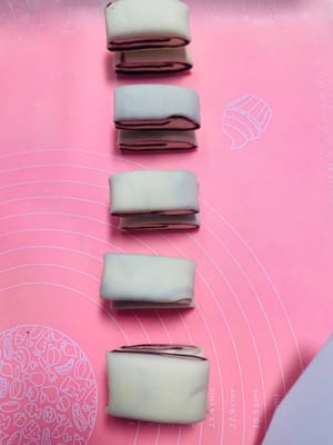 生地を幅の異なる2種類の細長い帯状に切ります。大きい方の帯は約3.5cm幅、小さい方の帯は約2cm幅です。小さい方の帯を大きい方の帯の上に重ねます。