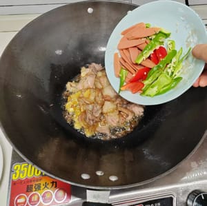 Agregue 5 rodajas de ajo a la carne magra marinada y saltee uniformemente, luego agregue el pimiento verde y la salchicha de jamón y continúe salteando.