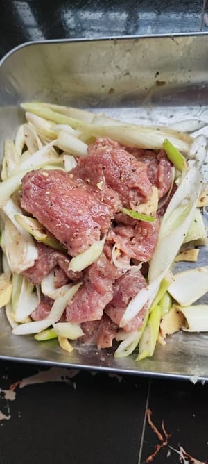 Utilisez du papier absorbant pour essuyer la viande lavée, faites mariner les oignons verts hachés, le gingembre râpé, la quantité appropriée de fécule de maïs, 15 ml de sauce soja, 10 ml de vin de cuisine, 2 grammes de sel, 20 grammes de poivre noir, 15 ml d'huile de cuisson, mélangez bien et laissez mariner pendant 10 minutes
