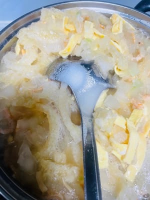 Ajoutez l’eau de trempage des crevettes séchées et des pétoncles dans la casserole. Si elle est insuffisante, ajoutez un peu d’eau bouillante (du bouillon est préférable). Laissez mijoter environ 10 minutes pour bien cuire le melon d’hiver. Ajoutez ensuite les lanières de couenne d’œuf et de porc et poursuivez la cuisson 5 minutes supplémentaires pour bien mélanger les ingrédients. Salez à votre goût.