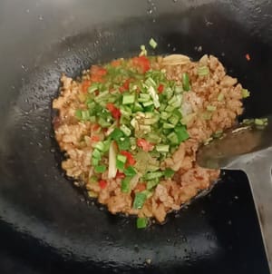 Grüne und rote Paprika und Schalotten dazugeben und gleichmäßig unter Rühren anbraten.