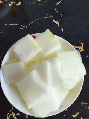 Zuerst das Fruchtfleisch der Wintermelone putzen. Anschließend die Schale abziehen und in grobe Würfel schneiden.
