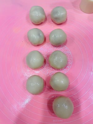 包月饼
取一个冰皮小团,用手压扁,把它压成一个圆饼。然后把搓好的馅料球放在中间,像包包子一样把口收起来,再搓圆。尽量搓成有点椭圆形,这样等下压模的时候不容易露边。