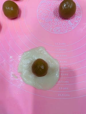 Preparazione del Mooncake
Prendete un pezzetto di pasta sfoglia e appiattitelo con le mani fino a formare una torta rotonda. Quindi, posizionate la pallina di ripieno al centro, ripiegate la parte superiore come un panino e arrotolatela fino a ottenere una forma rotonda. Cercate di renderla leggermente ovale in modo che i bordi non si vedano quando la modellate.