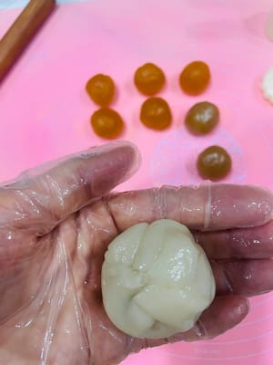 Preparazione del Mooncake
Prendete un pezzetto di pasta sfoglia e appiattitelo con le mani fino a formare una torta rotonda. Quindi, posizionate la pallina di ripieno al centro, ripiegate la parte superiore come un panino e arrotolatela fino a ottenere una forma rotonda. Cercate di renderla leggermente ovale in modo che i bordi non si vedano quando la modellate.