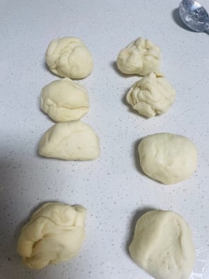 Dividere l'impasto in piccoli pezzi e lasciarli lievitare: Cospargere di farina il piano di lavoro, prendere l'impasto e dividerlo in piccoli pezzi di circa 45 g, formare delle palline, coprire con pellicola e lasciar lievitare per 15 minuti per far 