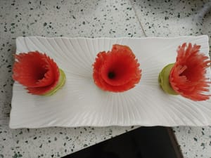 Die Karottenscheiben zu kleinen Blüten falten und auf die Gurkenringe legen