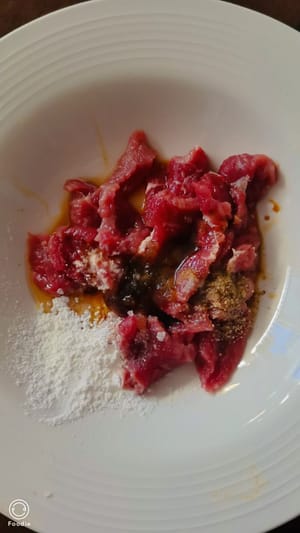 Das Rindfleisch waschen, Sehnen und Häute entfernen und in dünne Scheiben (etwa so dick wie eine Münze) schneiden. Die Rindfleischscheiben kurz mit 5 ml warmem Wasser, 2 g Pfeffer, 1 TL Speisestärke, etwas Zucker, 1 TL heller Sojasauce, 1/2 TL Austernsauce, 1/2 TL Speiseöl und etwas Salz marinieren. 3 bis 4 Minuten ziehen lassen.