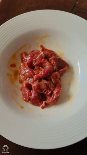 Das Rindfleisch waschen, Sehnen und Häute entfernen und in dünne Scheiben (etwa so dick wie eine Münze) schneiden. Die Rindfleischscheiben kurz mit 5 ml warmem Wasser, 2 g Pfeffer, 1 TL Speisestärke, etwas Zucker, 1 TL heller Sojasauce, 1/2 TL Austernsauce, 1/2 TL Speiseöl und etwas Salz marinieren. 3 bis 4 Minuten ziehen lassen.