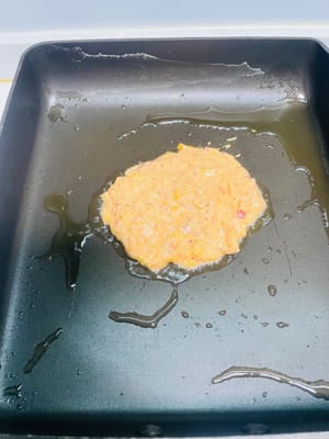 Cottura in padella delle frittelle: Scaldare abbondante olio in una padella, versare un cucchiaio di pastella e stenderla delicatamente con una spatola fino a formare una frittella rotonda. Friggere fino a quando un lato è cotto e i bordi sono dorati, quindi girare la frittella e friggere l'altro lato fino a quando entrambi i lati sono croccanti e dorati.