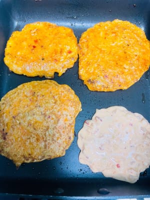 Cottura in padella delle frittelle: Scaldare abbondante olio in una padella, versare un cucchiaio di pastella e stenderla delicatamente con una spatola fino a formare una frittella rotonda. Friggere fino a quando un lato è cotto e i bordi sono dorati, quindi girare la frittella e friggere l'altro lato fino a quando entrambi i lati sono croccanti e dorati.