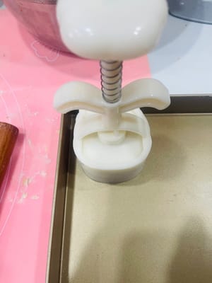 First, sprinkle some dry flour inside the mooncake mold to prevent sticking.
Place the wrapped mooncake balls on a baking sheet, carefully covering them with the mooncake mold. Hold the mold firmly with your hand and press down gently. The beautiful mooncake dough will emerge.