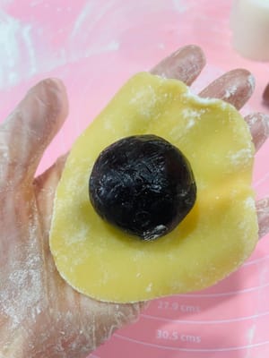 3. Wrapping the Mooncakes (Watch Video)
1. Divide the rested mooncake dough into 30g balls, roll them into balls, and flatten them.
2. Place the prepared red bean paste, egg yolk, and pork floss filling in the center of the mooncake wrapper. Wrap it up like a bun, seal the top with your thumb and index finger, and then roll it into a ball.
3. Sprinkle flour on the surface of the mooncake, tap off any excess, and place it on a baking sheet.