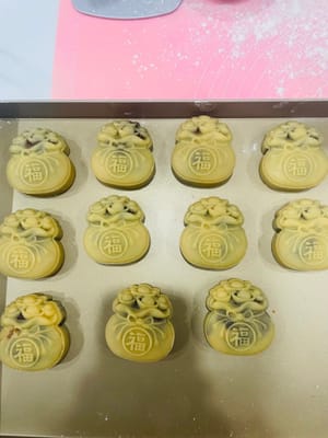 먼저 월병 틀 안에 밀가루를 살짝 뿌려 달라붙지 않도록 합니다.
포장된 월병을 베이킹 시트에 놓고 월병 틀로 조심스럽게 덮습니다. 손으로 틀을 단단히 잡고 살살 눌러줍니다. 아름다운 월병 반죽이 완성됩니다.