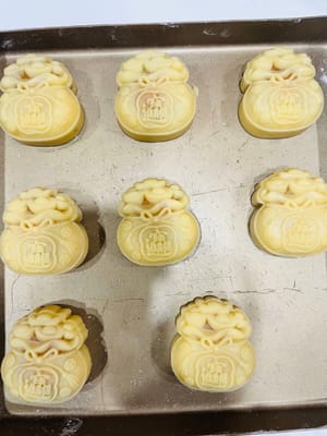 First, sprinkle some dry flour inside the mooncake mold to prevent sticking.
Place the wrapped mooncake balls on a baking sheet, carefully covering them with the mooncake mold. Hold the mold firmly with your hand and press down gently. The beautiful mooncake dough will emerge.