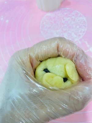 3. Wrapping the Mooncakes (Watch Video)
1. Divide the rested mooncake dough into 30g balls, roll them into balls, and flatten them.
2. Place the prepared red bean paste, egg yolk, and pork floss filling in the center of the mooncake wrapper. Wrap it up like a bun, seal the top with your thumb and index finger, and then roll it into a ball.
3. Sprinkle flour on the surface of the mooncake, tap off any excess, and place it on a baking sheet.