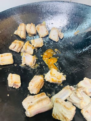 Friture et coloration : Graisser la poêle avec de l'huile pour éviter qu'elle ne colle. Ajouter les travers de porc et les faire frire jusqu'à ce qu'ils soient dorés des deux côtés. Ajouter le sucre candi jaune et faire frire jusqu'à ce que le sucre se colore, donnant aux travers de porc une belle couleur et un arôme caramélisé.
