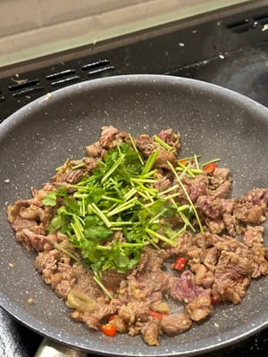 Korianderwurzeln und Salz hinzufügen, weiter braten, bis die Wurzeln weich sind