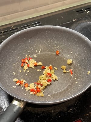 In einer erhitzten Pfanne kleine rote Chilischoten, eingelegte Chilischoten, Knoblauch und Ingwer 2 Minuten anbraten
