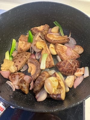 Eine Pfanne erhitzen und Ingwer, Frühlingszwiebeln, Knoblauch und Schalotten darin anbraten, bis sie duften. Shiitake-Pilze hinzufügen und unter Rühren braten, bis die Flüssigkeit verdampft ist. Das Einweichwasser der Shiitake-Pilze dazugeben.
