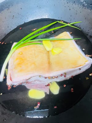 Selezionate la pancetta di maiale alternando strati di grasso e carne magra. Per prima cosa, bruciacchiate la pelle del maiale per rimuovere l'odore di pesce e i peli. Quindi, mettetela in una pentola di acqua fredda con cipollotti, vino da cucina, grani di pepe e fette di zenzero per sbollentarla. Dopo che l'acqua bolle, cuocetela per circa 25 minuti, quindi scolatela e lavatela per un uso successivo.