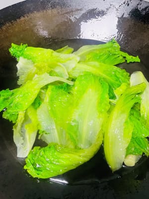Agregue la lechuga escurrida, déle la vuelta rápidamente con palillos, blanquéela durante 30 segundos a 40 segundos, retírela rápidamente del plato y colóquela en un plato, luego vierta la salsa previamente preparada uniformemente sobre la lechuga y un plato de deliciosa lechuga blanqueada al estilo cantonés está listo.