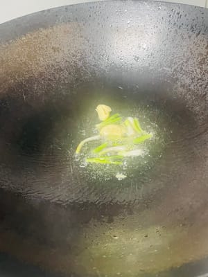 Vierta una cantidad adecuada de aceite de cocina en la sartén y caliéntelo a fuego medio-bajo. Cuando el aceite esté caliente, añada el ajo y los gajos de cebolleta. Saltee hasta que el ajo esté ligeramente dorado y los gajos de cebolleta desprendan su aroma, para realzar el aroma.