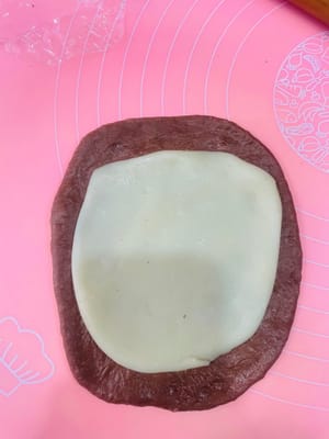 包餡整形:
取一個鬆弛好的麵團擀開,麻薯也擀薄點(比面皮小一圈就行),鋪在麵團上,撒上愛吃的堅果,再塞3-4個法芙娜巧克力幣(我主打一個摳搜,只放3個也超香!)。接著捲緊捲實,別讓餡料半路「離家出走」~