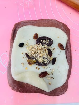 包餡整形:
取一個鬆弛好的麵團擀開,麻薯也擀薄點(比面皮小一圈就行),鋪在麵團上,撒上愛吃的堅果,再塞3-4個法芙娜巧克力幣(我主打一個摳搜,只放3個也超香!)。接著捲緊捲實,別讓餡料半路「離家出走」~