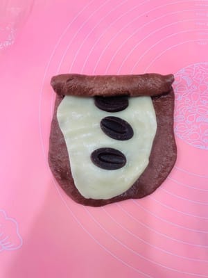 包餡整形:
取一個鬆弛好的麵團擀開,麻薯也擀薄點(比面皮小一圈就行),鋪在麵團上,撒上愛吃的堅果,再塞3-4個法芙娜巧克力幣(我主打一個摳搜,只放3個也超香!)。接著捲緊捲實,別讓餡料半路「離家出走」~