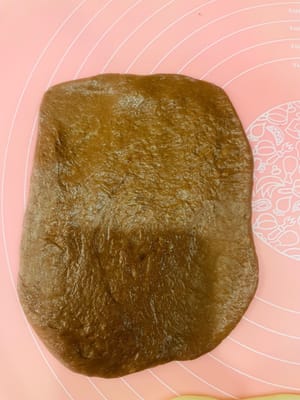 包餡整形:
取一個鬆弛好的麵團擀開,麻薯也擀薄點(比面皮小一圈就行),鋪在麵團上,撒上愛吃的堅果,再塞3-4個法芙娜巧克力幣(我主打一個摳搜,只放3個也超香!)。接著捲緊捲實,別讓餡料半路「離家出走」~