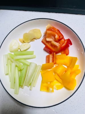 Den Sellerie in Stücke, die Paprika in kleine Würfel, den Ingwer in Scheiben und den Knoblauch in flache Stücke schneiden.