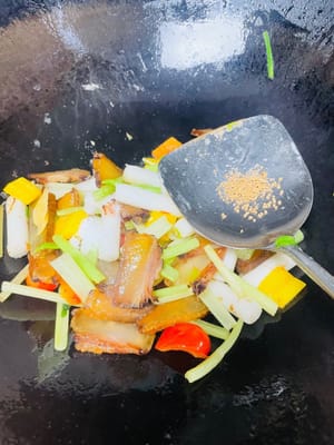 Knoblauch, Ingwer, Sellerie (falls nicht benötigt), eingeweichten Reiskuchen und Paprika hinzufügen. Bei mittlerer bis niedriger Hitze 3–4 Minuten anbraten. Da Speck von Natur aus salzig ist, nur 1 Teelöffel Salz verwenden. Mit 1 Teelöffel Hühnerbrühe würzen.