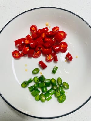 Ingwer in Scheiben oder Streifen schneiden, Knoblauch zerdrücken und fein hacken. Grüne und rote Chilischoten klein schneiden. Für später beiseitestellen.