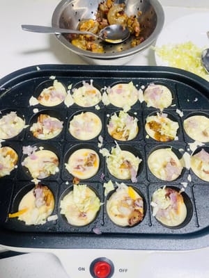 반죽 붓기: 작은 구멍에 반죽을 반쯤 채우고, 양념한 새우와 오징어 다리를 넣은 다음, 다진 양파와 다진 양배추를 넣습니다.