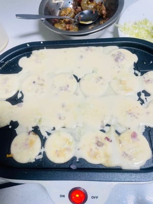 반죽 붓기: 작은 구멍에 반죽을 반쯤 채우고, 양념한 새우와 오징어 다리를 넣은 다음, 다진 양파와 다진 양배추를 넣습니다.