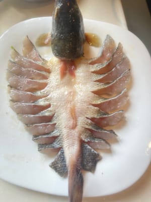 这一步很关键。把腌制好的鱼摆在一个宽大碟里。把鱼条扭一下，鱼皮往上面翻。把鱼头两只耳朵。鱼头跟鱼尾对直。摆好之后，喷一点油。来点姜片。准备蒸。