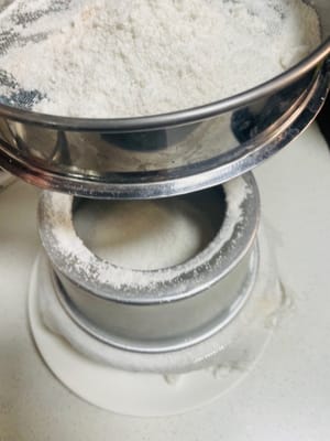 1. Die Hälfte des restlichen Pulvers auf das Käsetuch in der Form sieben.

2. Die Mischung aus schwarzem und weißem Sesampulver zusammen sieben und als zweite Schicht verwenden.

3. Die restliche Klebreismehlmischung in die Form sieben.

Diesen Vorgang insgesamt dreimal wiederholen. Die Form nach jeder Schicht leicht schütteln, um die Oberfläche zu glätten. Das Pulver nicht andrücken, da es sonst zu fest wird. Dieser Vorgang erfordert etwas Geduld und dauert etwa 10 Minuten.