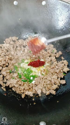 Ingwer, Frühlingszwiebeln und Bohnenpaste hinzufügen und unter Rühren braten, bis es duftet.