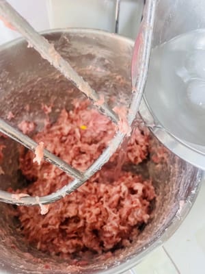 加入冰水:
分3次加冰水,每次加1/3,攪到肉把水全「吸」進去了再加下一次,全程得順著一個方向攪,攪到肉發黏、插根筷子能立住(這叫「上勁」,是Q彈的關鍵!不攪上勁煮出嚟就是散的)。